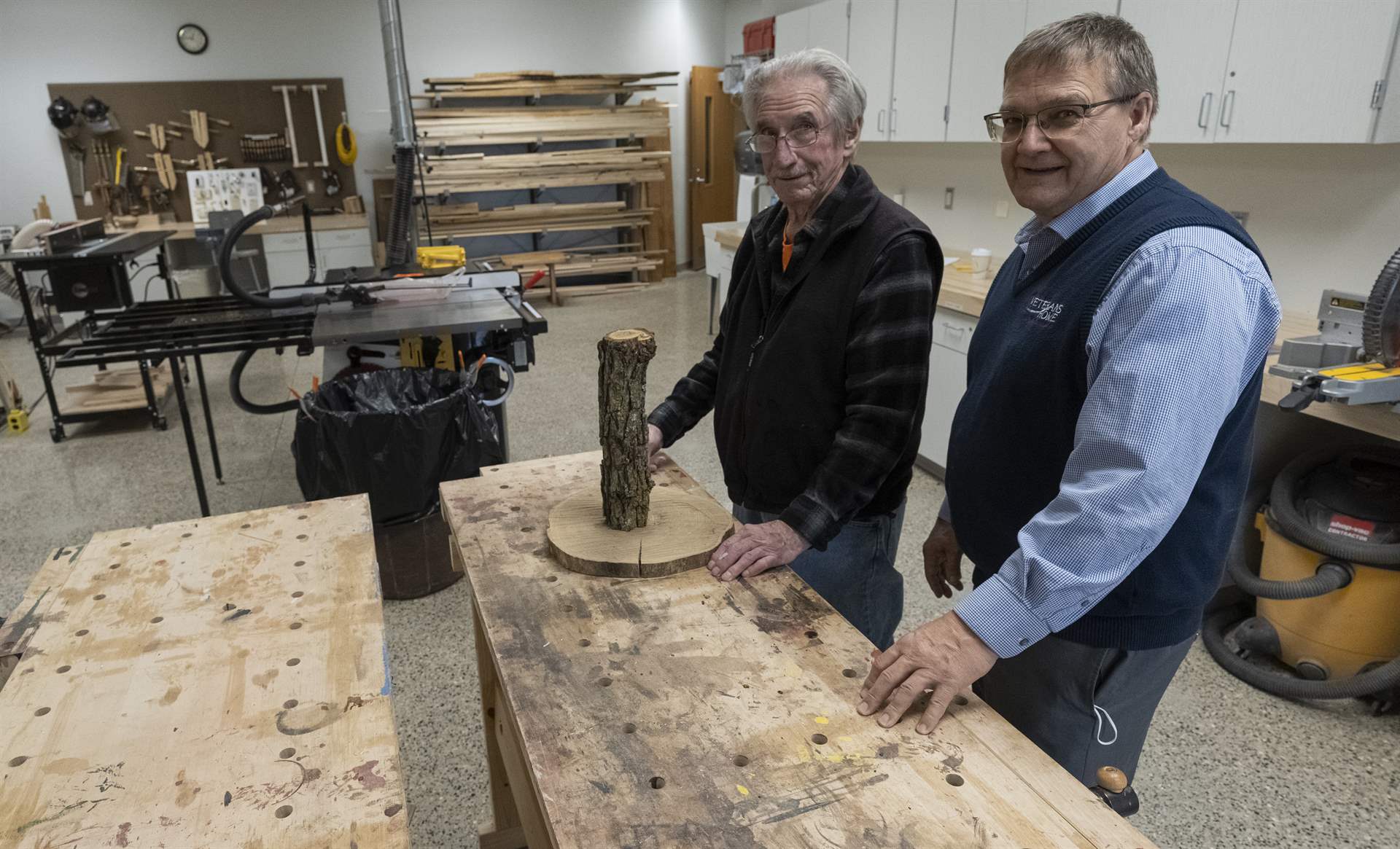 A resident and staff member of the North Dakota Veterans Home standing next to a workbench in the woodshop.